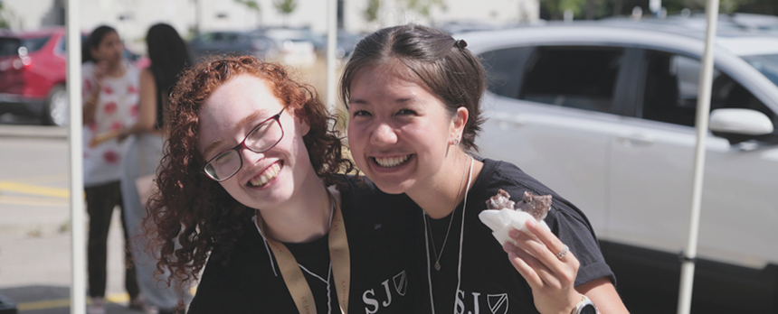 Two students smiling and eating a donut at orientation on St. Jerome's campus