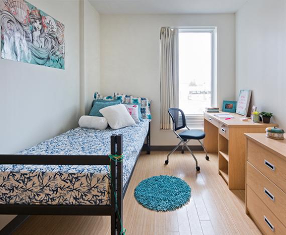 One of our residence rooms prepared with a desk, chair, bed and a window overlooking the campus, ready for you to move in and call it home.